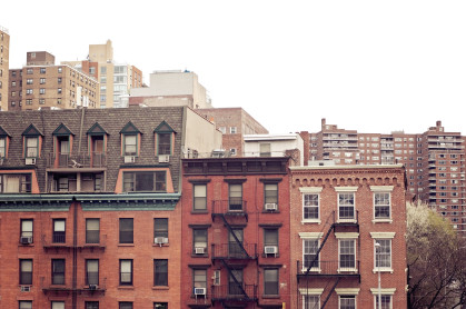 Three brownstone buildings in Manhattan backed by larger apartment complexes.