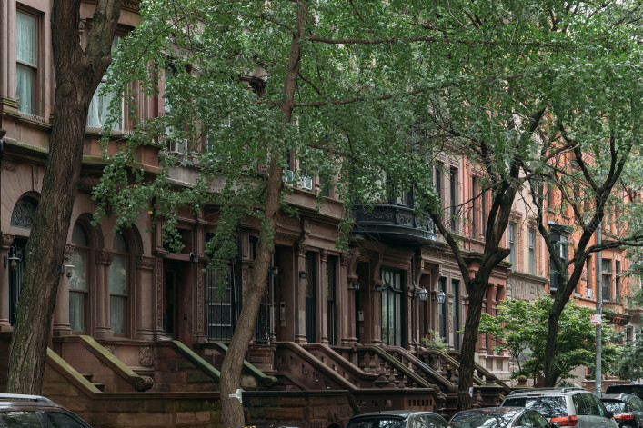 A picturesque view of classic brownstone buildings with lush trees in a serene New York City neighborhood.