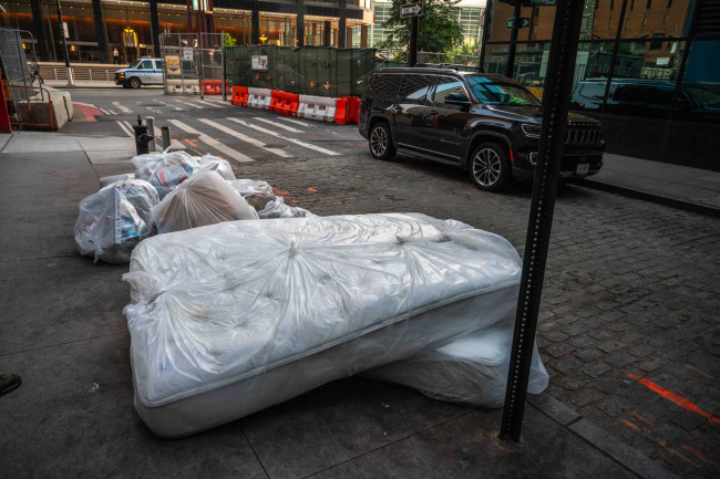 New York, NY, USA 07-18-2023 Mattresses wrapped in plastic on sidewalk out for trash with garbage bags on a Manhattan street. Editorial use only.