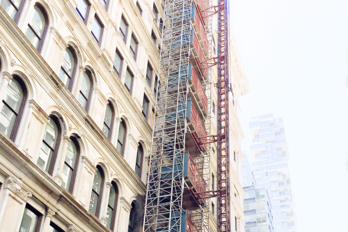 Scaffolding running up older building facade in Manhattan, NYC with newer buildings fading to white in the distance