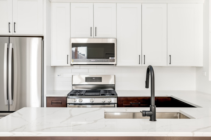 Contemporary kitchen design with white shaker style cabinets and white counters and backsplash. Small kitchen in city apartment.