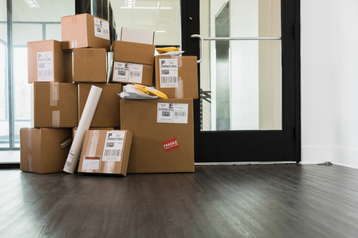 A large stack of cardboard boxes, envelopes and a cylinder are sitting inside a door of a building