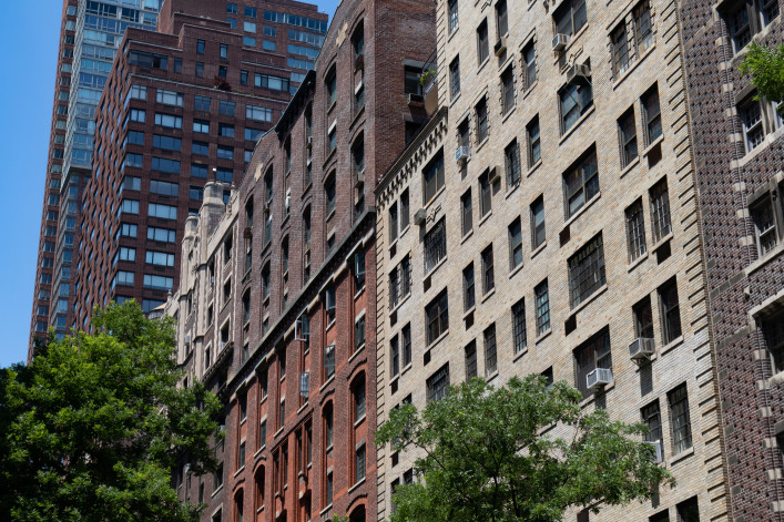 A row of old brick apartment building skyscrapers along a street on the Upper West Side of New York City