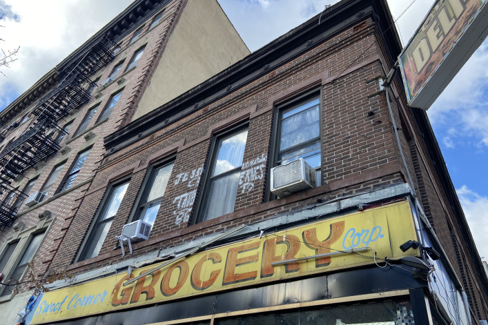 New York, NY USA - December 6, 2023 : Hand-painted yellow and red "Sweet Corner Grocery Corp." sign over a deli on a two-story brick apartment building in Harlem, New York City