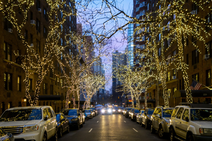 New york city street and brownstone buildings with trees covered in Christmas white lights one point perspective car dusk or early morning stock photo