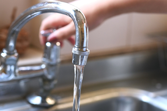 faucet with hand of woman in kitchen for cleaning, drinking and washing dishes. Interior, steel and household plumbing with sink and tap at home for stream, flowing and splash