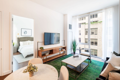 living room with brown sofa, green carpet, & large windows looking out on another Manhattan building