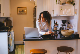 A young lady studying at the kitchen counter, utilizing a laptop and notepad.