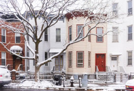 This is a front view of several residential buildings side by side along a street with snow on a winter day in Brooklyn, New York.