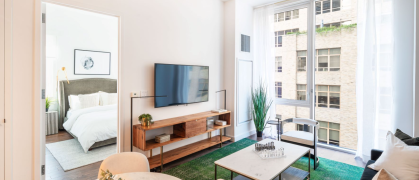 living room with brown sofa, green carpet, & large windows looking out on another Manhattan building