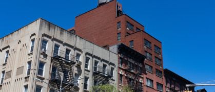 A row of colorful old brick apartment buildings with fire escapes along a street with a stop light on the Upper East Side of New York City