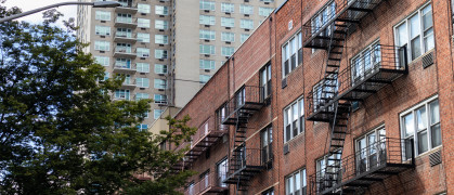 A row of old brick apartment buildings with fire escapes along a residential street on the Upper East Side of New York City