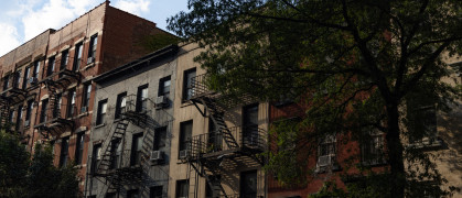 A row of colorful old brick apartment buildings and residential buildings with fire escapes along a street in Chelsea of New York City.