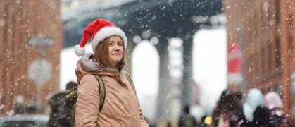 A young woman in a Santa Claus hat walks during a snowfall in NYC with Manhattan Bridge in the background