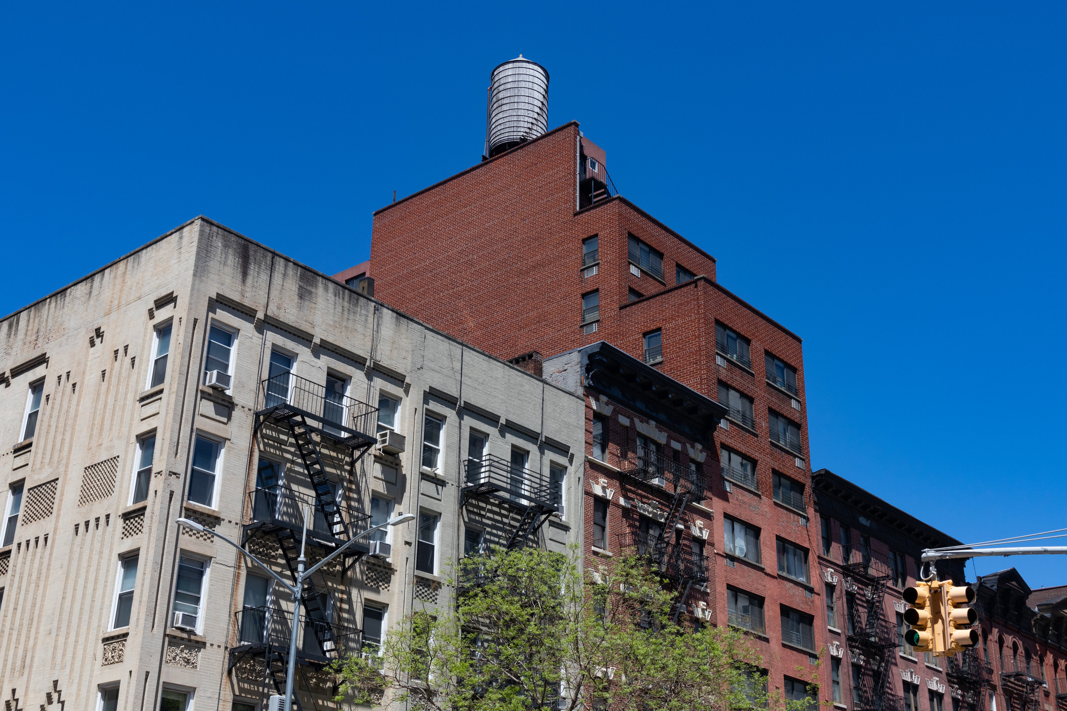 A row of colorful old brick apartment buildings with fire escapes along a street with a stop light on the Upper East Side of New York City