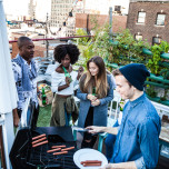 Friends having fun, grilling BBQ and drinking beers together during a rooftop party in New York East Village.